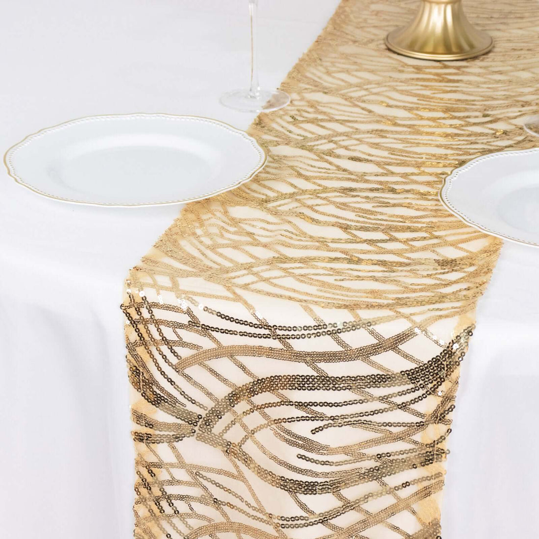 Gold beaded table runner on a white tablecloth with plates and glassware.