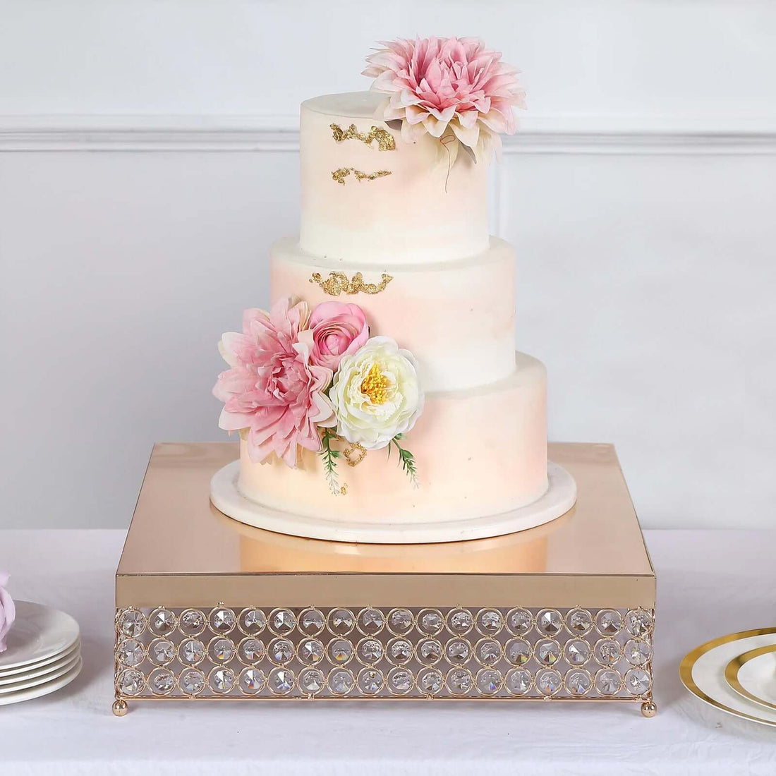 Elegant three-tiered wedding cake adorned with pink flowers and gold accents.