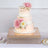 Elegant three-tiered wedding cake adorned with pink flowers and gold accents.