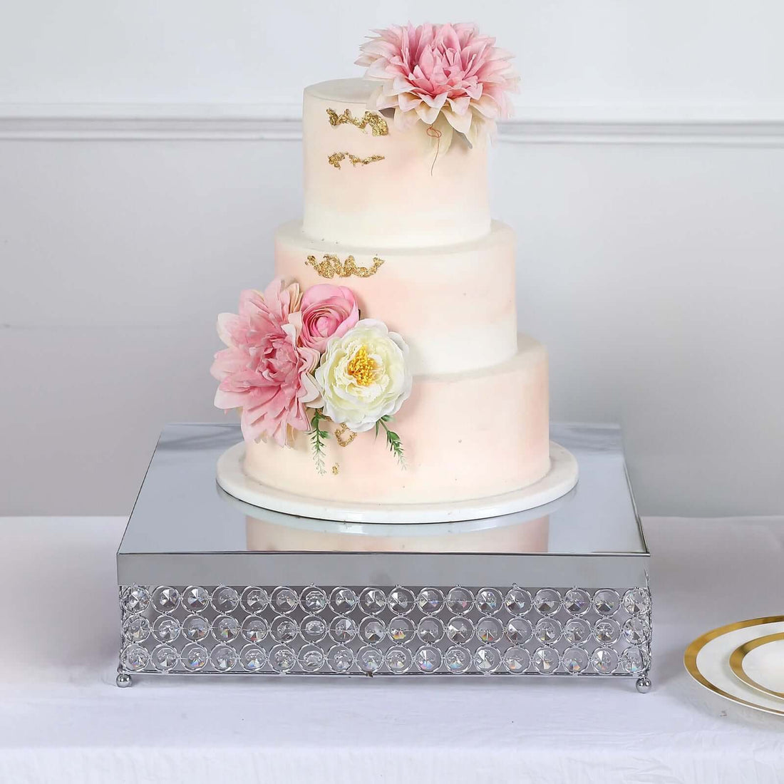Three-tiered wedding cake adorned with pink and white flowers on a mirrored base.