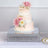 Three-tiered wedding cake adorned with pink and white flowers on a mirrored base.