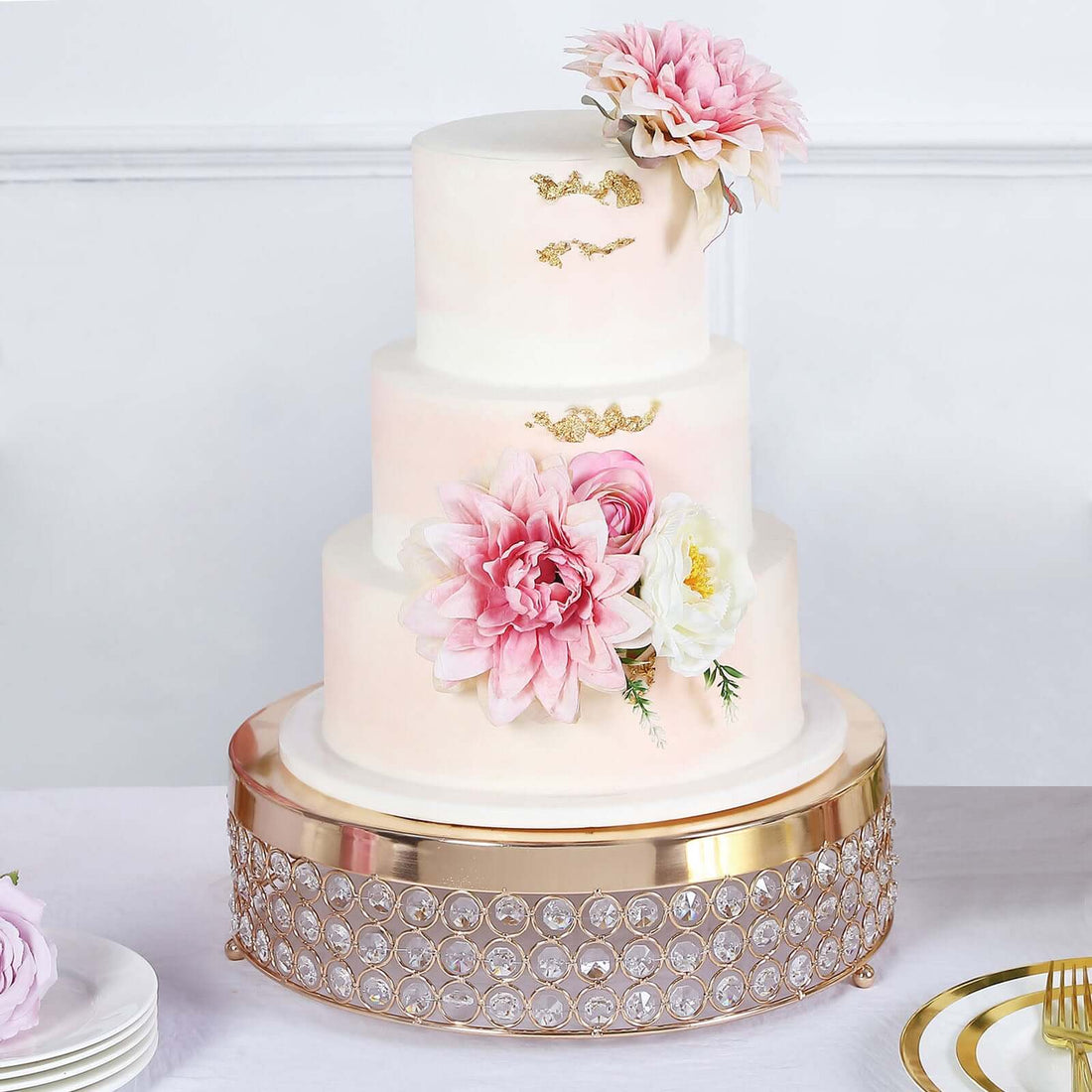 Elegant three-tier wedding cake adorned with pink flowers and gold accents.