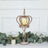 Gold crown candle holder with a white candle, surrounded by greenery.