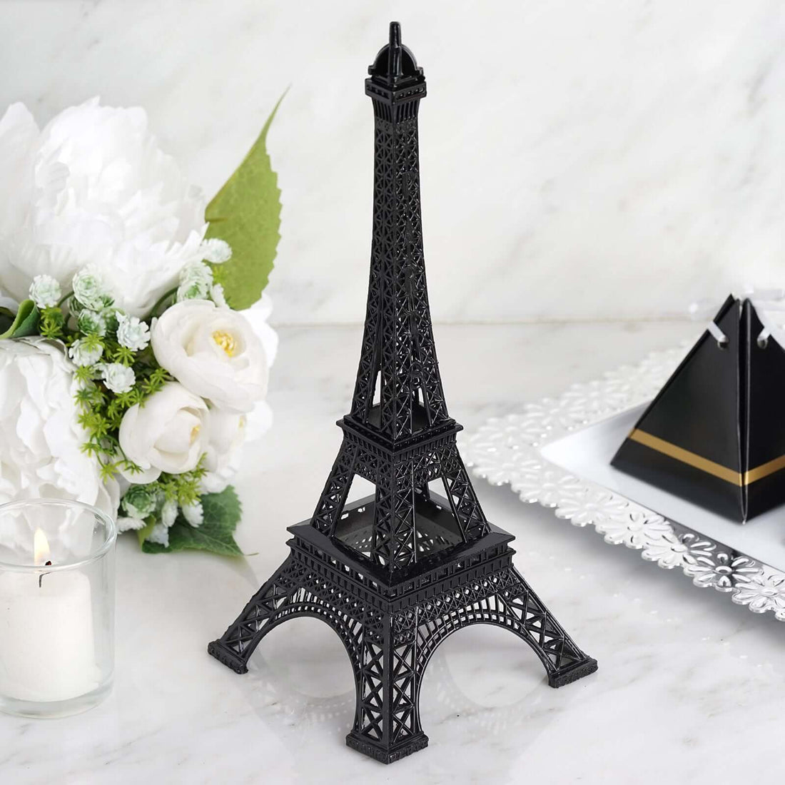 Black Eiffel Tower replica on a marble surface with flowers and dessert in the background.