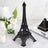 Black Eiffel Tower replica on a marble surface with flowers and dessert in the background.