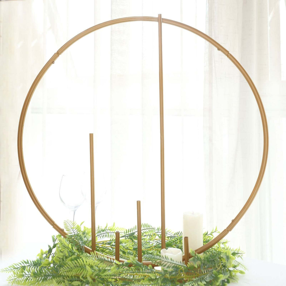 Gold circular candle holder with greenery and candles, studio shot.