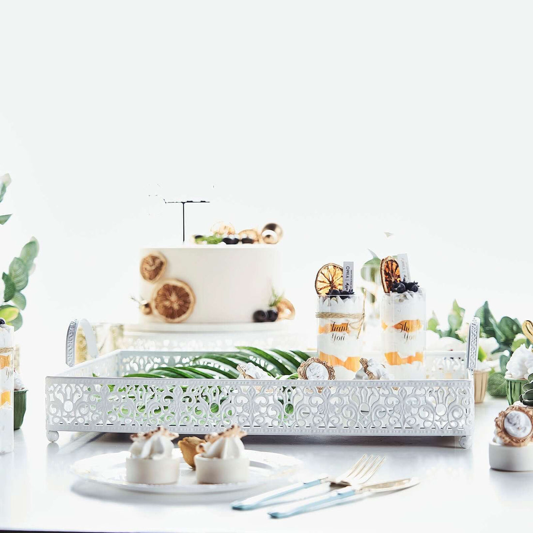 Elegant silver serving tray with desserts and floral decorations on a white backdrop.