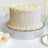 Elegant white cake with decorative frosting on a silver stand, set on a table.
