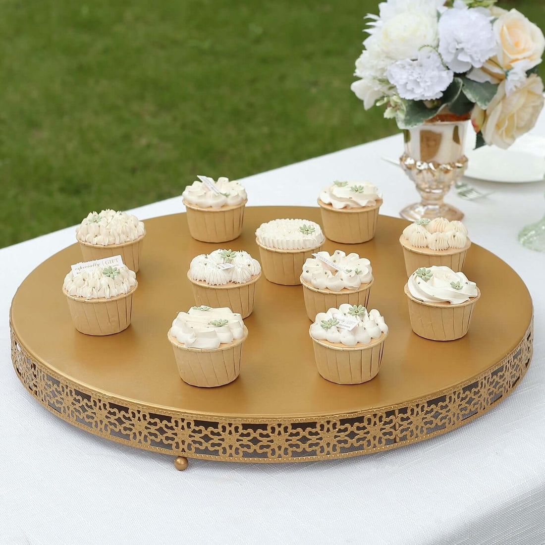 Decorative cupcakes on a gold platter at an outdoor event.