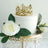 Elegant white cake with gold crown and floral decorations on a decorative stand.