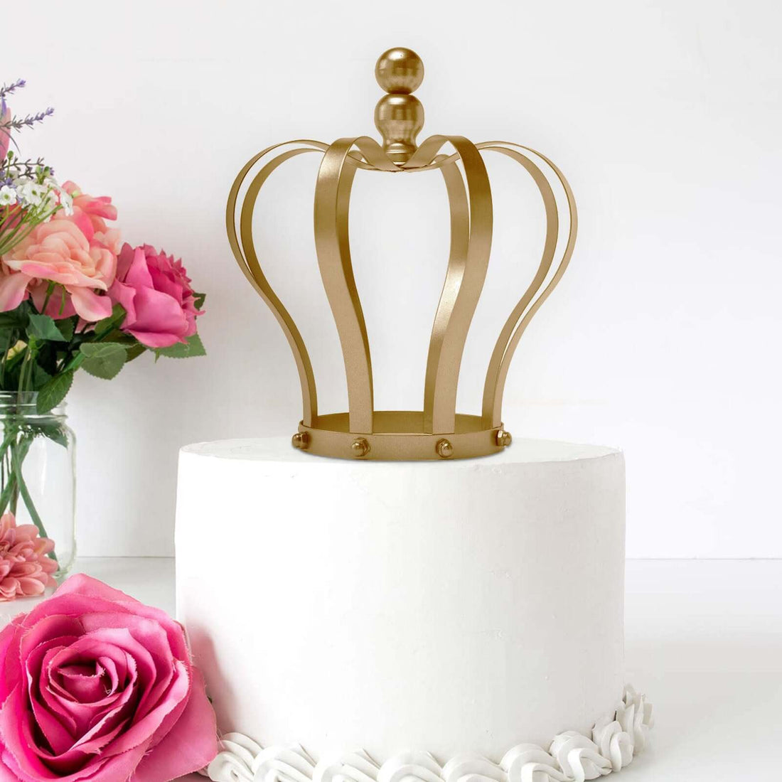 Gold crown cake topper on a white cake with pink flowers in the background.