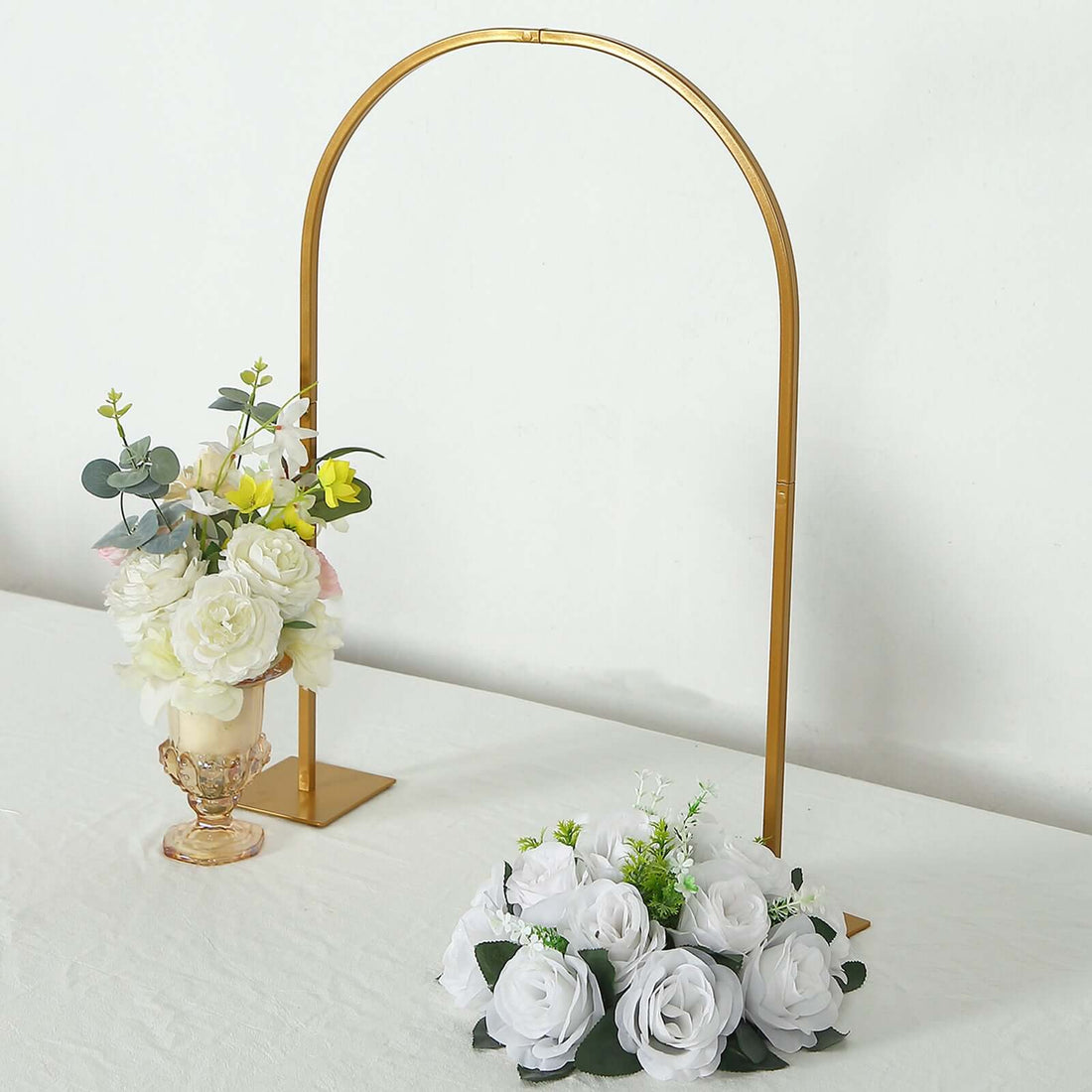 Gold arch floral display with white roses and greenery arrangements.