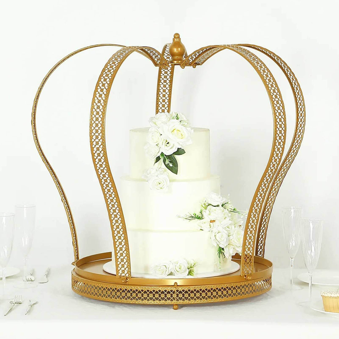Gold crown cake stand with white floral decoration and a three-tiered cake