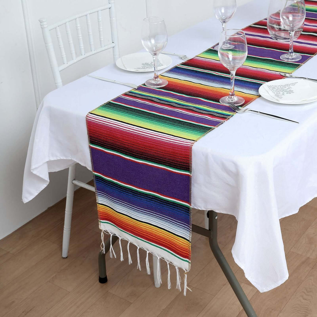 Colorful Mexican table runner on a dining table with plates and glasses.