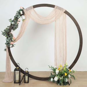 Decorative wedding arch with drapes, flowers, and lanterns on a neutral background.