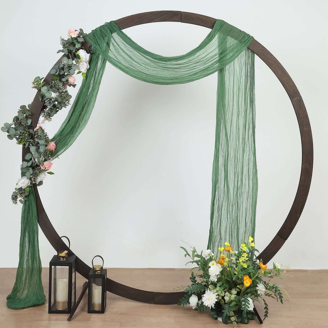 Green draped fabric with floral decor and lanterns in a circular wooden frame.