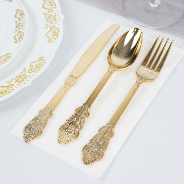 Gold cutlery set on a white napkin with decorative plate in the background.
