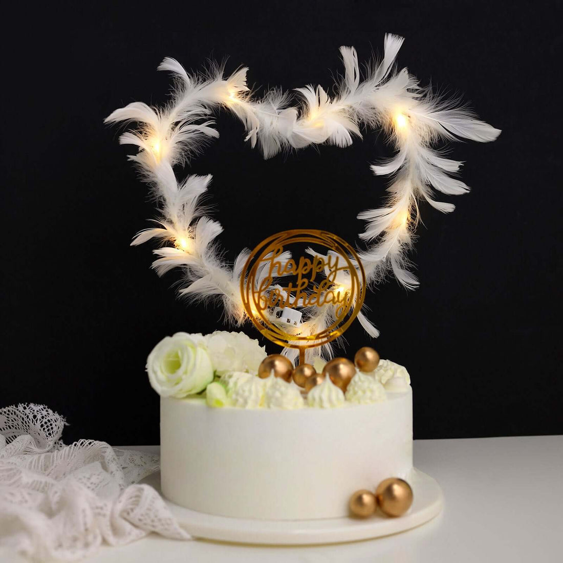 Birthday cake with heart-shaped feather decor and golden "Happy Birthday" sign.