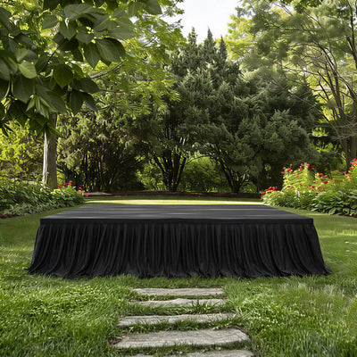 Outdoor black-draped stage in a lush garden with trees and flowers