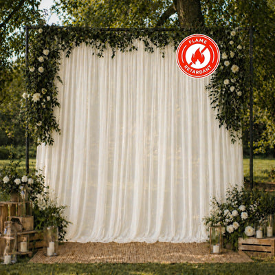 Outdoor wedding backdrop with white drapes, flowers, and flame retardant sign