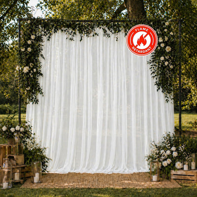 Outdoor wedding backdrop with white drapes, greenery, flowers, and candles