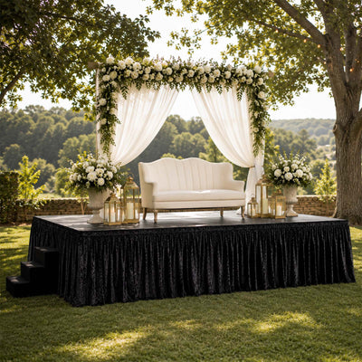 Outdoor wedding stage with floral arch, white loveseat, and lanterns under trees