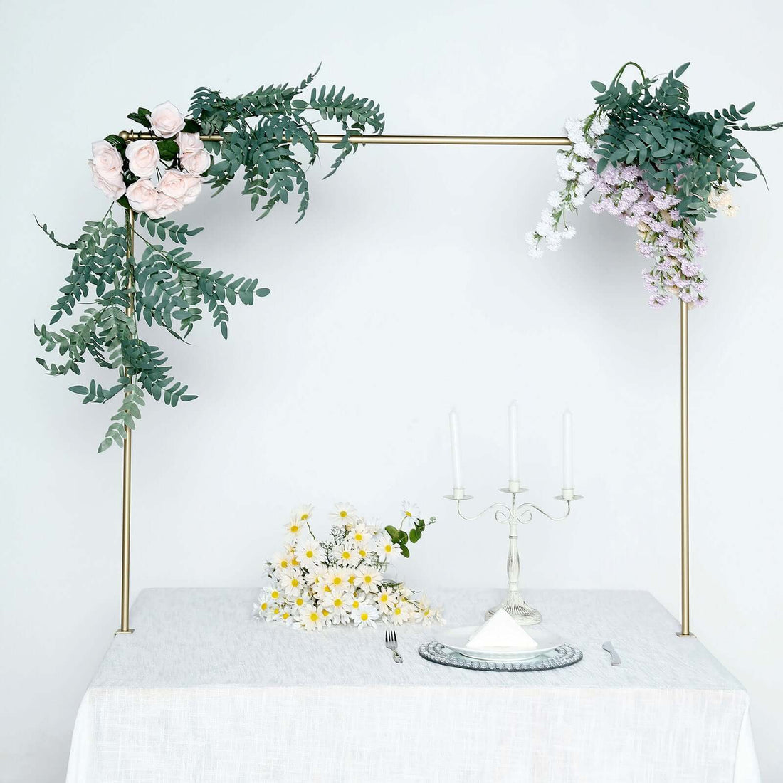 Elegant floral arch with white table setting and candles in a minimalist space.