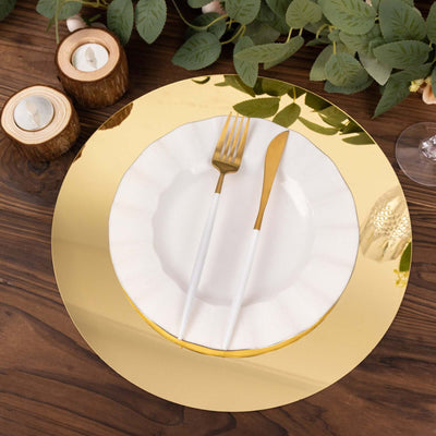 Gold charger plate with white ruffled plate and golden cutlery on a wooden table.
