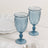 Blue glass goblets on a marble table with white plates and silverware.