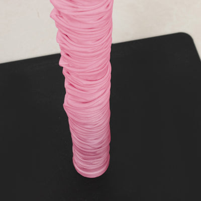 Pink ribbed fabric wrapped around a vertical cylinder on a black surface