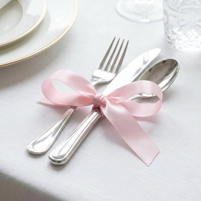 Pink ribbon tied around silver cutlery on elegant white table setting