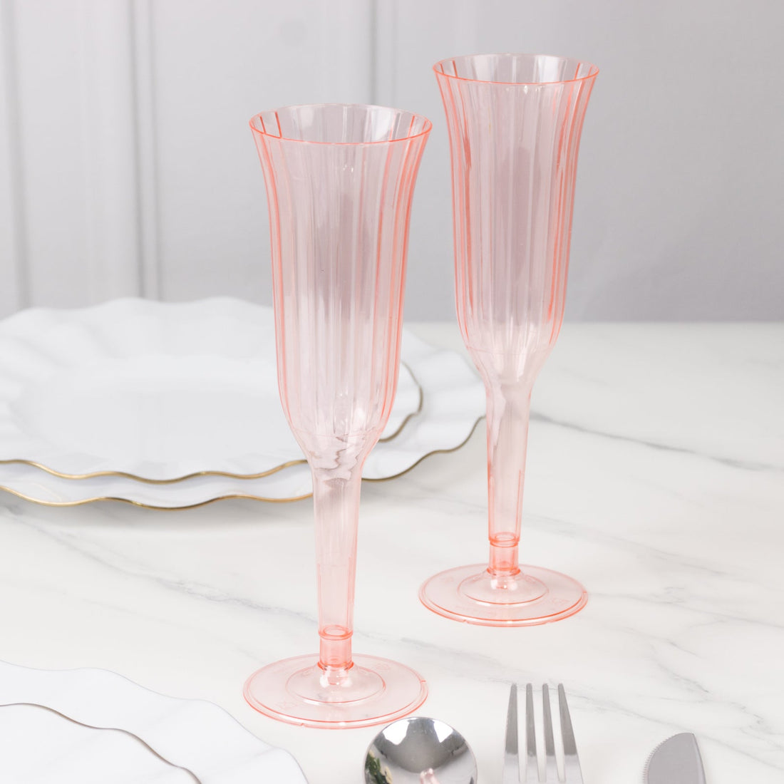 Pink ribbed champagne flutes on a marble table setting.