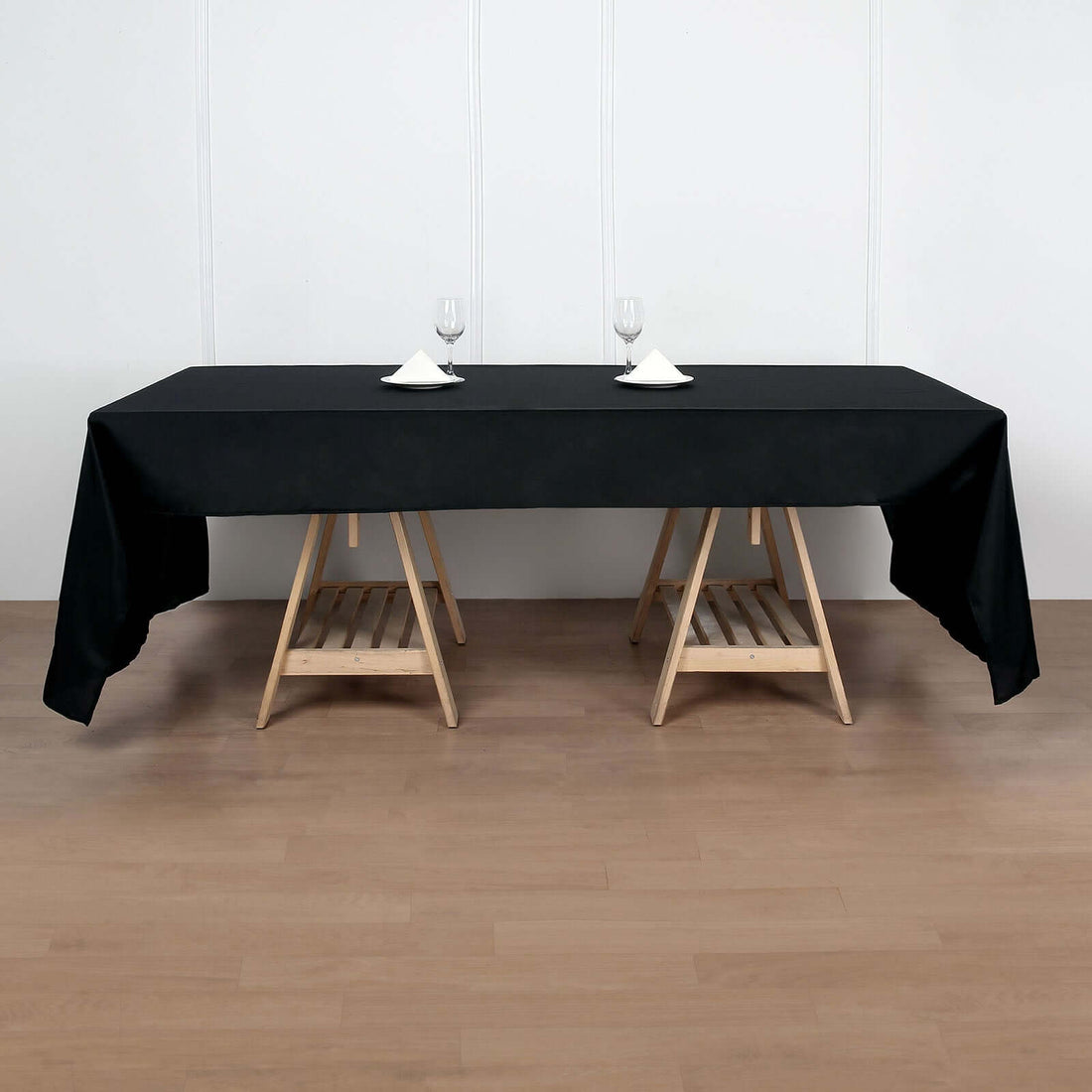 Black tablecloth draped over a wooden table with glasses and napkins