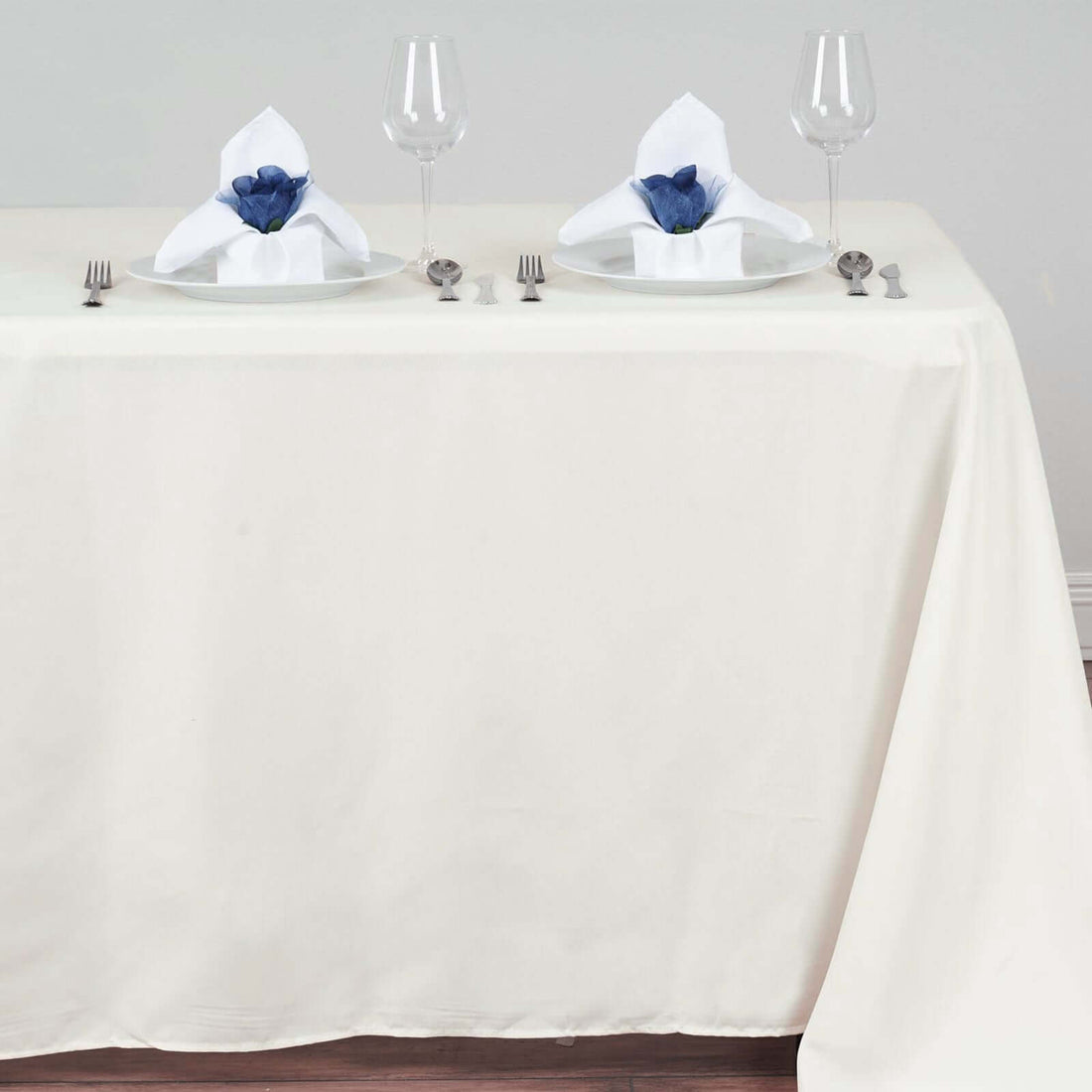 Elegant dining setup with white plates, blue napkins, and glasses on a cream tablecloth.