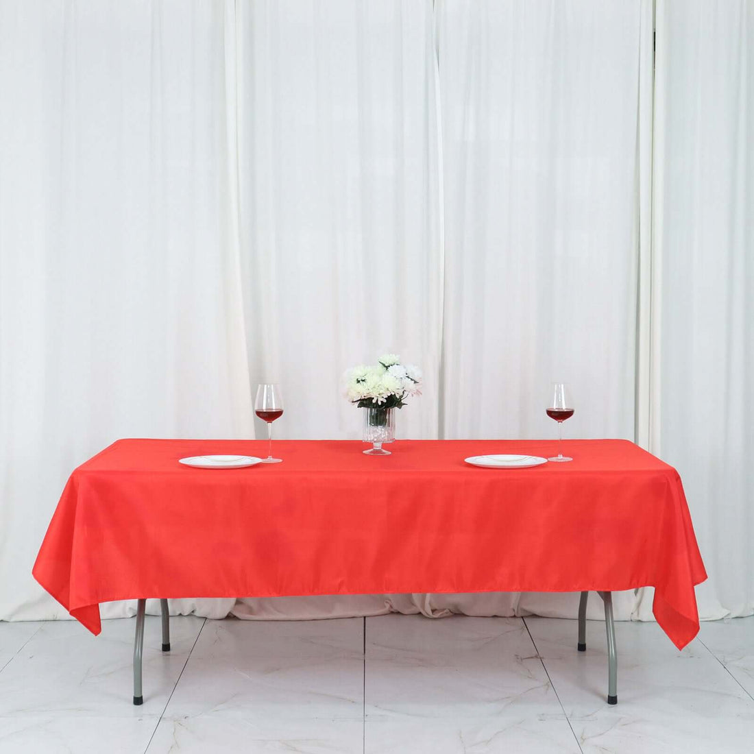 Red tablecloth elegantly draped on a table set for dinner with wine glasses and flowers.