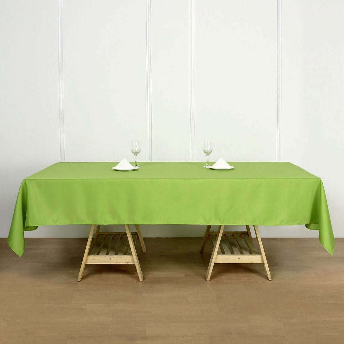 Green tablecloth draped over a wooden table with glassware and napkins.