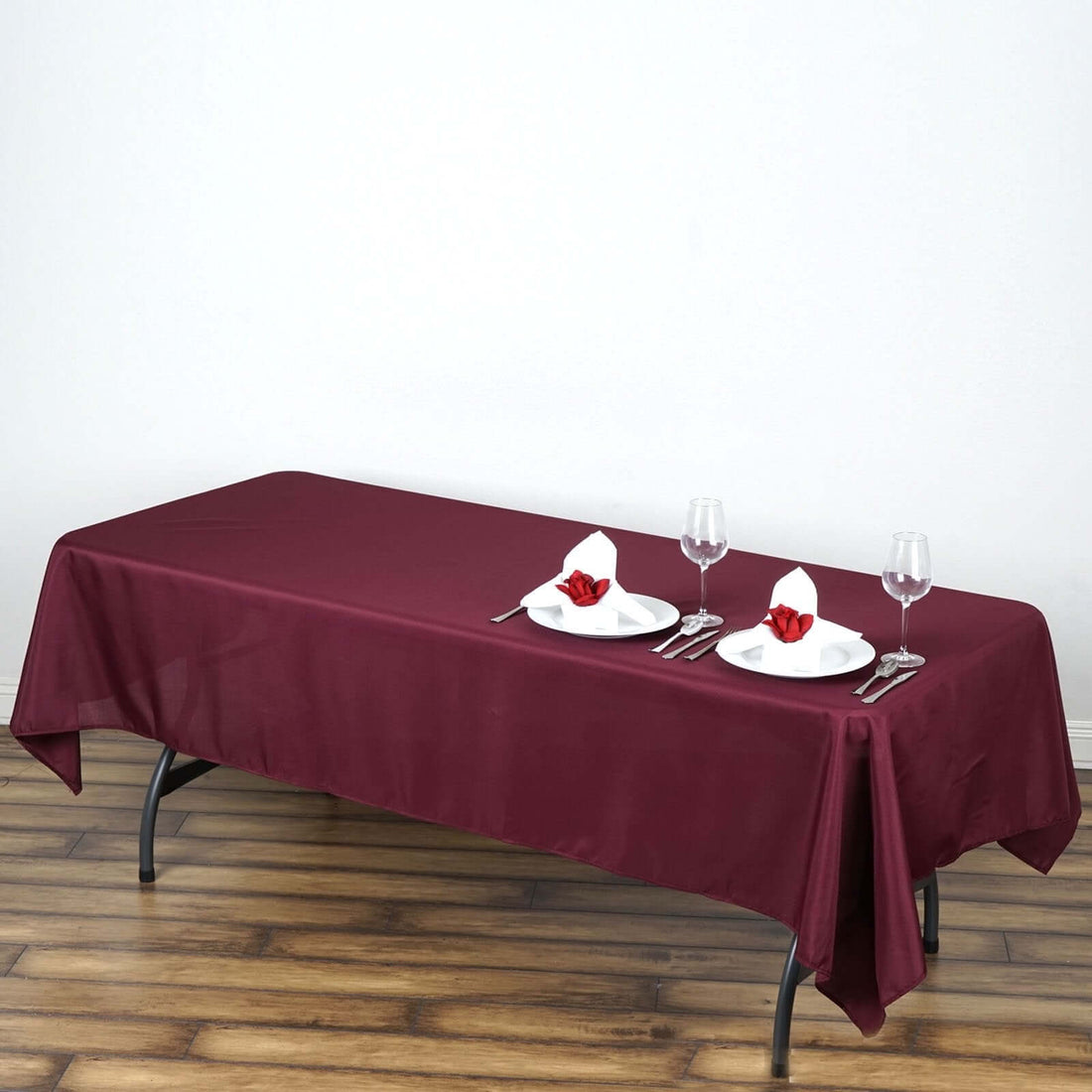 Burgundy tablecloth on a dining table set for a meal with plates and glasses.