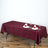 Burgundy tablecloth on a dining table set for a meal with plates and glasses.