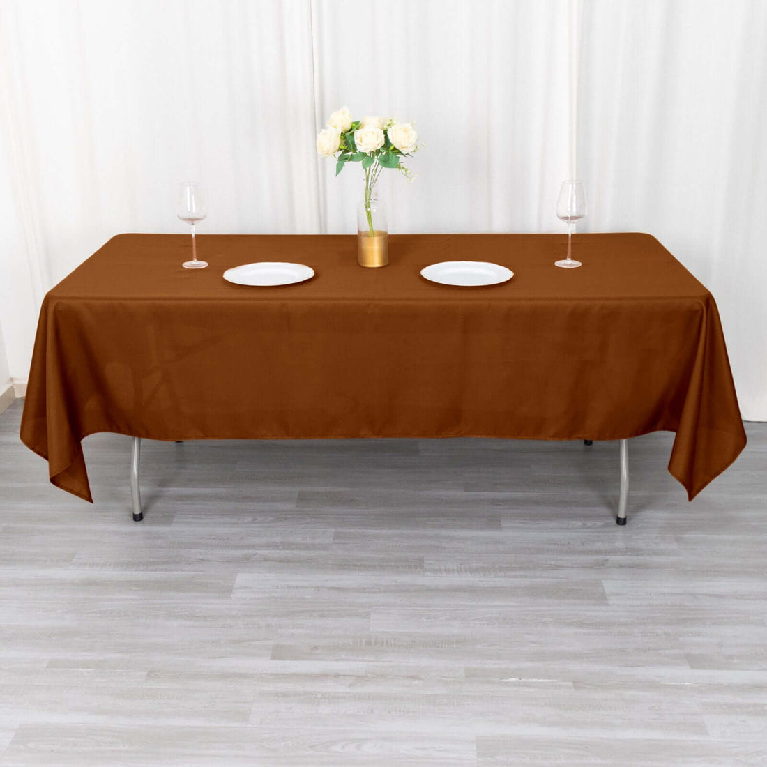 Brown tablecloth draped over a table with plates and a vase of flowers.