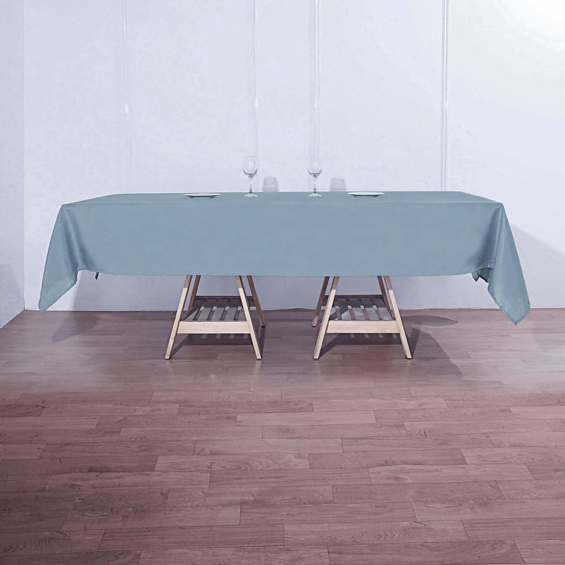 Rectangular table with a light blue tablecloth and glasses on a wooden floor.
