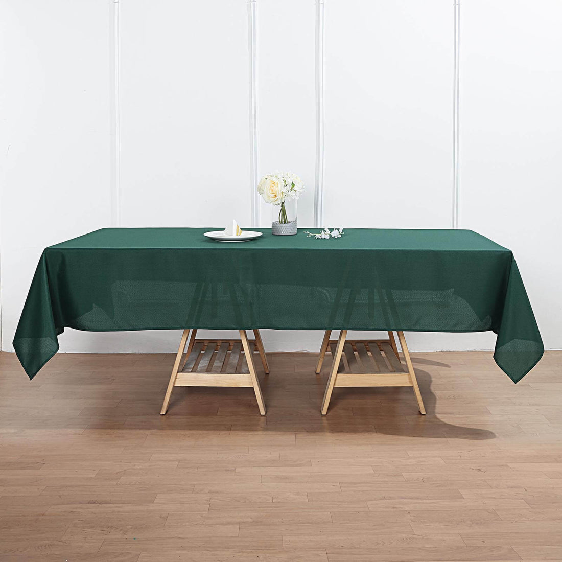 Green tablecloth draped on wooden table with floral centerpiece