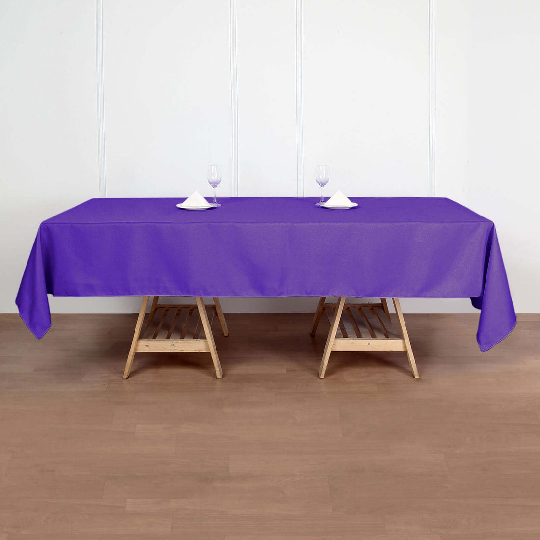 Purple tablecloth draped over a wooden table with glasses and napkins.