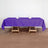 Purple tablecloth draped over a wooden table with glasses and napkins.