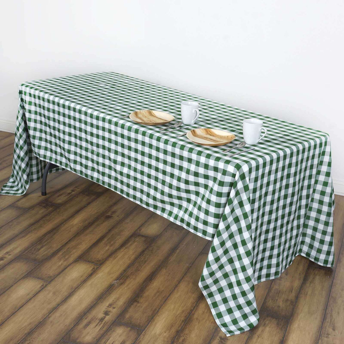 Green and white checkered tablecloth draped over a table with plates and mugs.