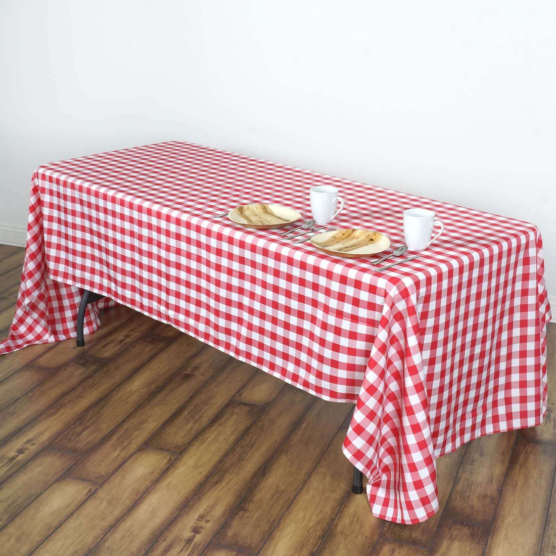 Red and white checkered tablecloth on a wooden table with plates and cups.