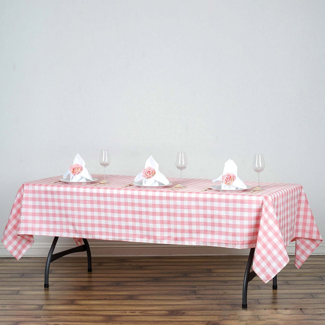 Pink checkered tablecloth set for dining with elegant napkins and glasses.