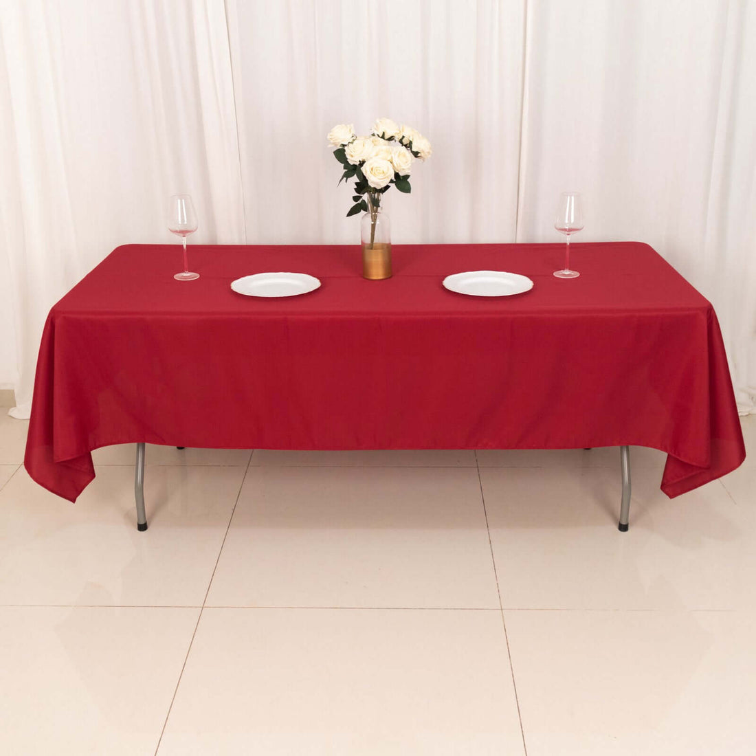 Red tablecloth draped over a table set with plates and glasses, decorated with flowers.