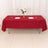 Red tablecloth draped over a table set with plates and glasses, decorated with flowers.