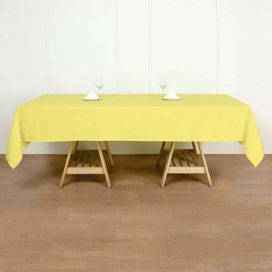 Yellow tablecloth draped over a wooden table with glasses and napkins.