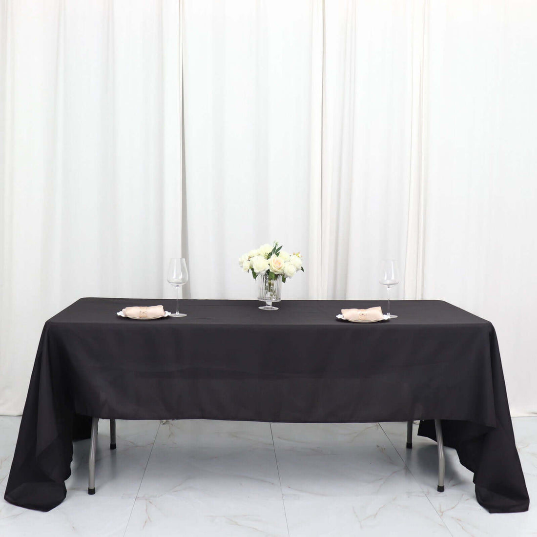 Black tablecloth elegantly draped on a table set for dining with flowers and glassware.